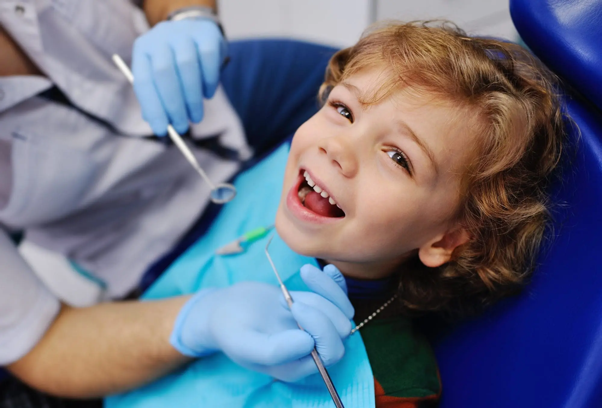 A young child, who appears to be of Caucasian descent based on their features and complexion, smiles during a dental exam. Limestone Hills Orthodontics in Austin, TX, offers pediatric care.