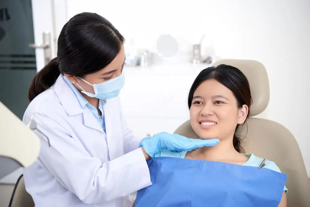 asian female dentist checking out patients teeth woman smiling - Dentofacial Orthopedics Explained: Growth Modification vs Tooth Movement | Limestone Hills Orthodontics Austin TX