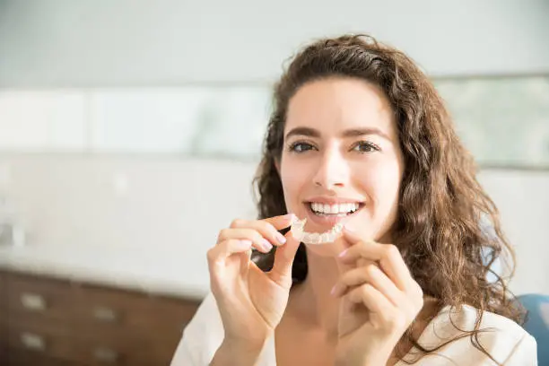 A smiling young woman, who appears to be of Caucasian descent based on her features, holds clear aligners. Limestone Hills Orthodontics in Austin, TX, offers Invisalign treatment.