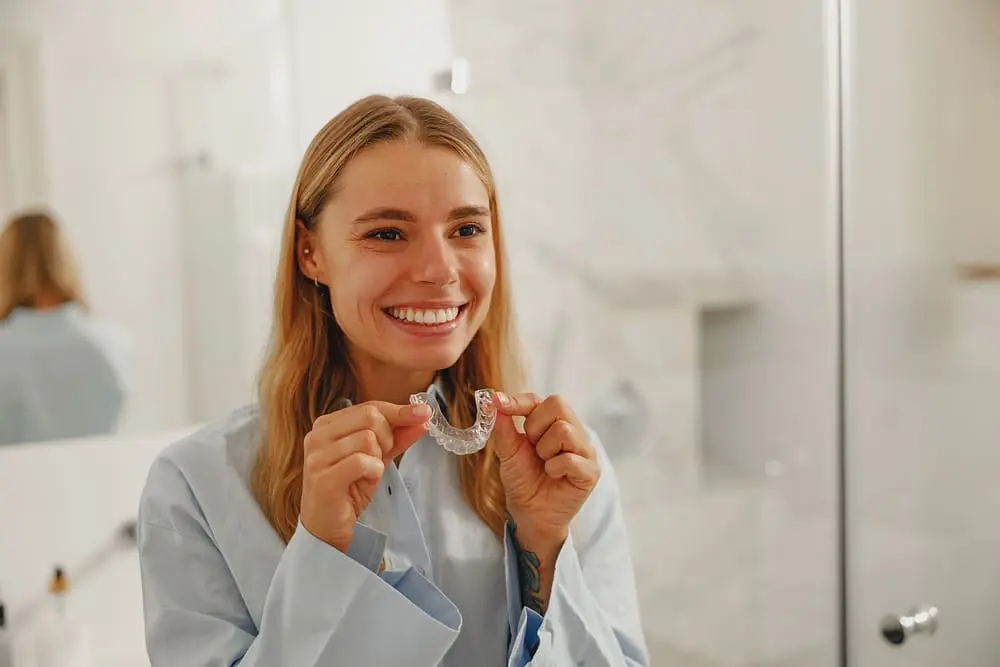 cheerful young woman proudly displaying her invisalign clear aligners - How to Clean Invisalign: The Daily and Weekly Protocol | Limestone Hills Orthodontics Austin TX 