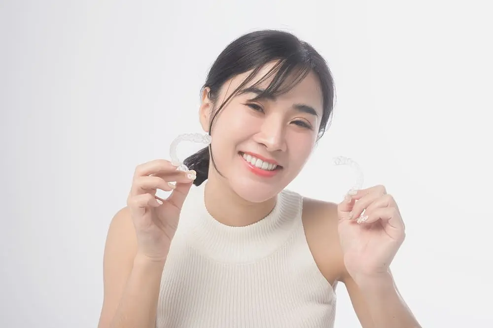 young smiling woman holding invisalign clear aligners white background - How to Clean Invisalign: The Daily and Weekly Protocol | Limestone Hills Orthodontics Austin TX