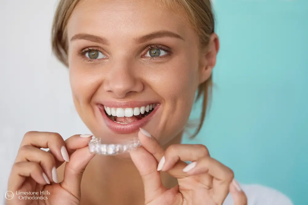 a woman smiling holding a clear plastic clear aligners vs Invisalign