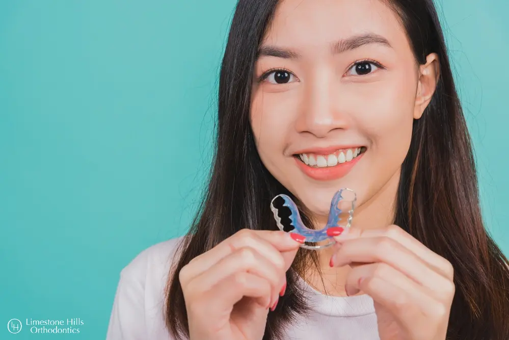 a woman smiling holding a blue retainer. Retainers vs Braces in Austin, TX