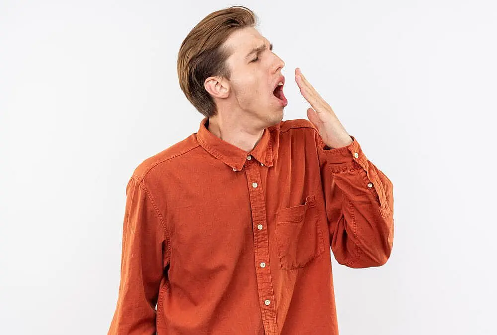 A young man, who appears to be of Caucasian ethnicity based on his features and complexion, is shown with his mouth wide open and his hand raised towards his mouth, possibly depicting mouth breathing. This image could be used to illustrate the concept of mouth breathing and its potential connection to the development of an underbite, a condition that Limestone Hills Orthodontics