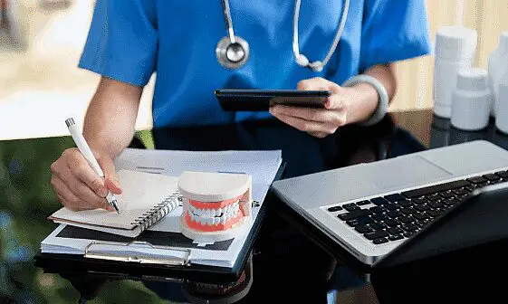 A dental professional, whose race and ethnicity are not discernible from the image, takes notes near a dental model and laptop. Limestone Hills Orthodontics in Austin, TX, focuses on patient care.