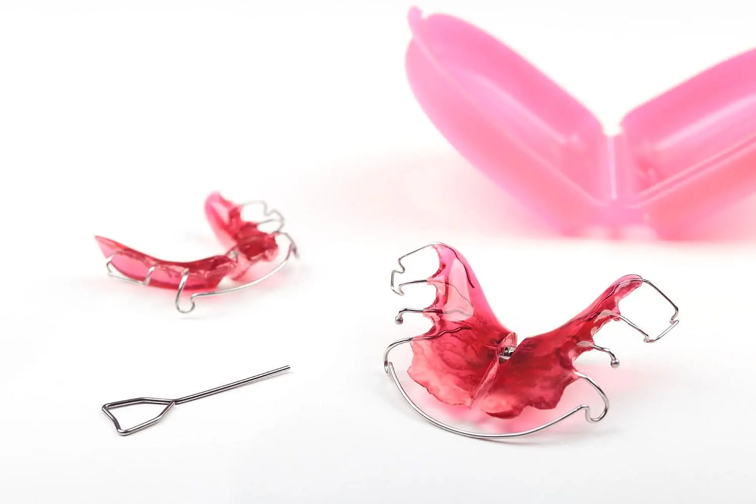 Two Hawley retainers, a removal tool, and a pink case are shown. Limestone Hills Orthodontics in Austin, TX, provides orthodontic aftercare.