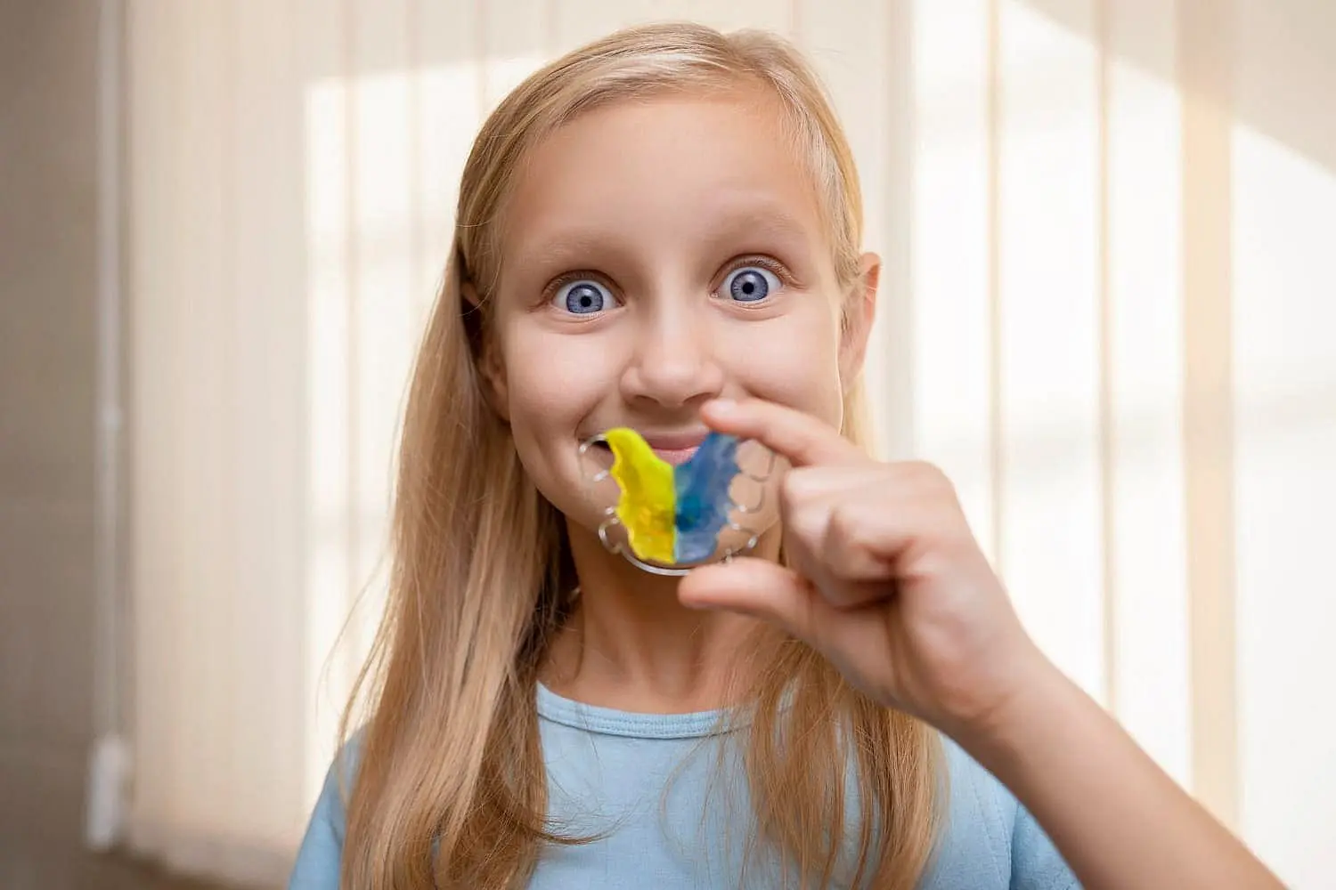 A young girl, who appears to be of Caucasian descent based on her features and complexion, holds a colorful orthodontic retainer. Limestone Hills Orthodontics in Austin, TX.
