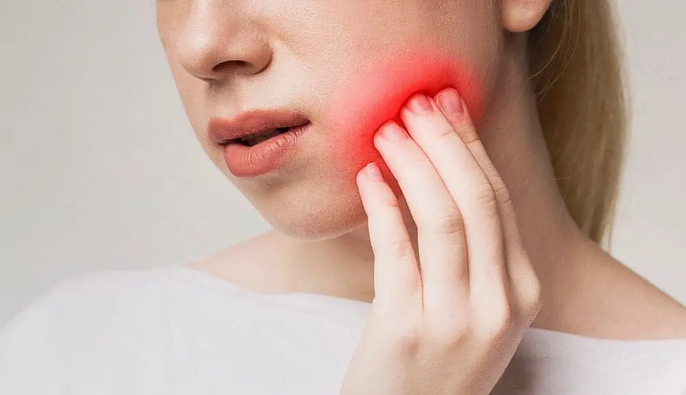 A woman, who appears to be of Caucasian descent based on her features and complexion, holds her jaw, highlighted in red, suggesting pain. Limestone Hills Orthodontics in Austin, TX, can assess jaw discomfort.