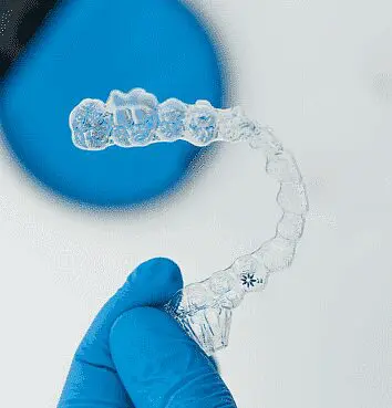 A gloved hand holds a clear Invisalign aligner. Limestone Hills Orthodontics in Austin, TX, offers Invisalign as an orthodontic treatment option.