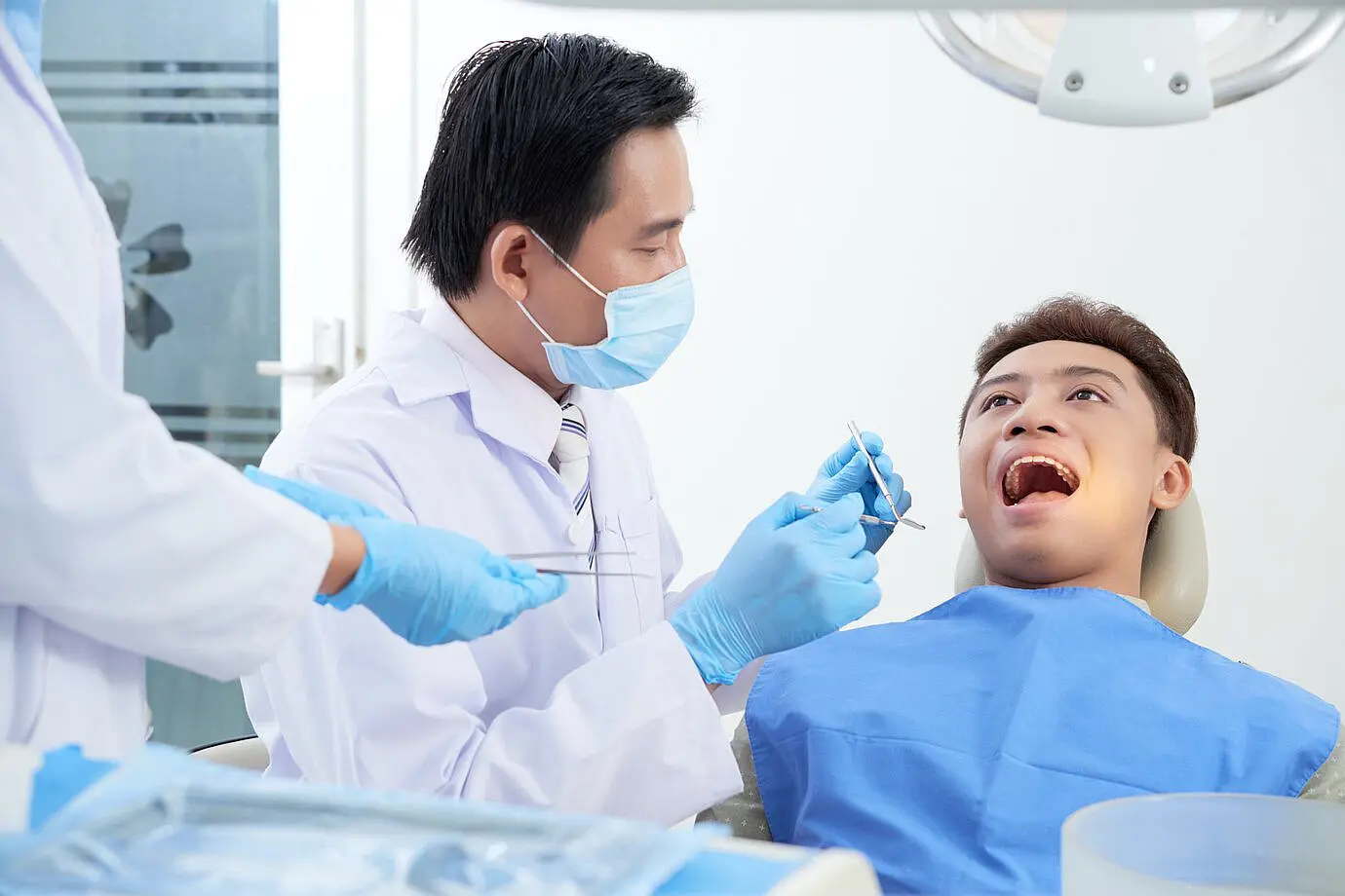 A dentist, who appears to be of Asian descent based on his features, examines a patient's open mouth. Limestone Hills Orthodontics in Austin, TX, offers orthodontic evaluations.