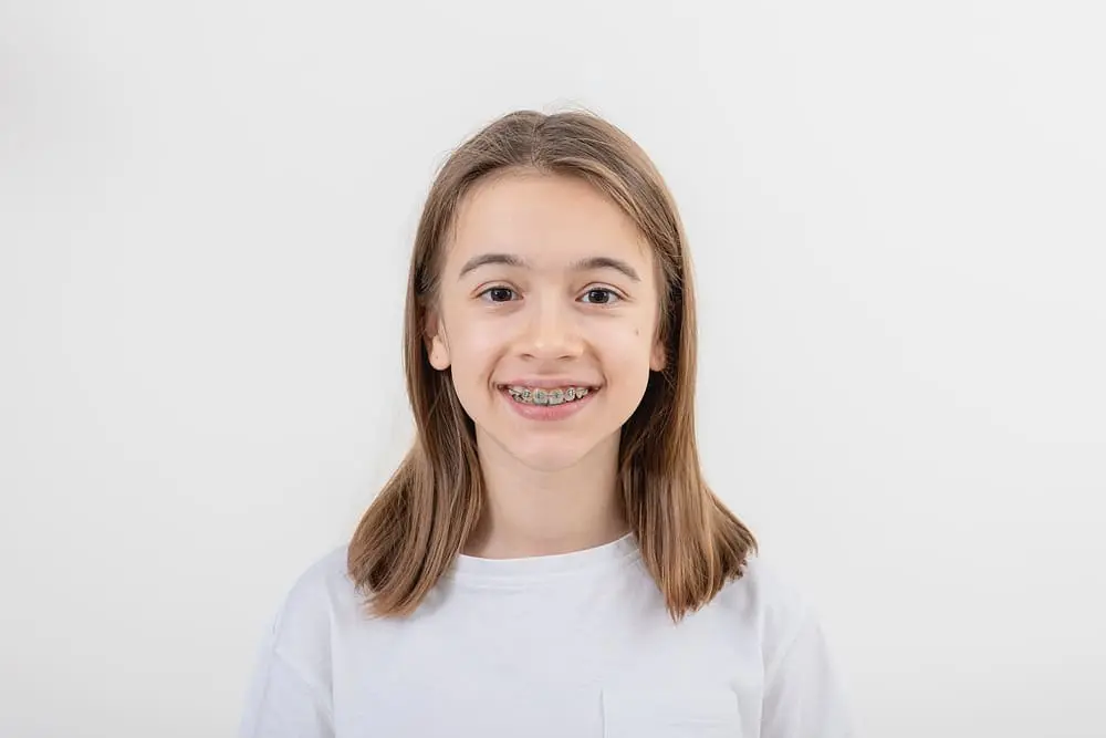 A young girl smiles, showing her braces, against a plain white backdrop in Austin, TX.