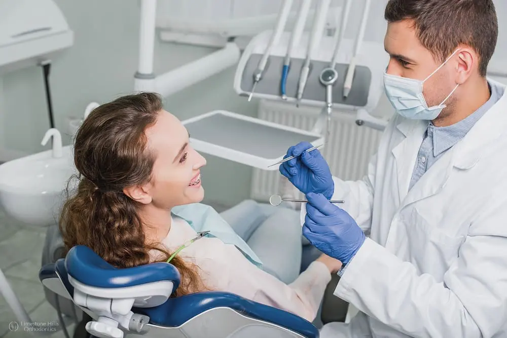 A dental professional, who appears to be a man and may be of Caucasian descent based on his features, examines a smiling young patient. Limestone Hills Orthodontics in Austin, TX, offers orthodontic care.