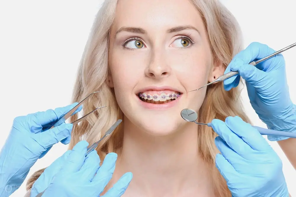 Hands holding dental tools near a smiling woman with metal braces, orthodontic treatment scene to explain are braces necessary