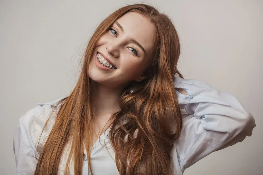 Happy young red-haired woman smiling with clear braces after she is free from risks of mail order orthodontics