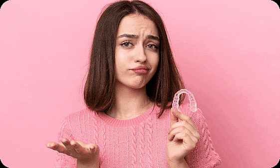 A young woman, who appears to be of Caucasian descent based on her features and complexion, looks uncertain while holding clear aligners. Limestone Hills Orthodontics in Austin, TX, can answer your questions.