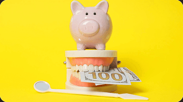 A piggy bank sits on a model of teeth with a $100 bill. A dental mirror is below. Limestone Hills Orthodontics in Austin, TX, discusses treatment costs.