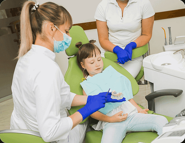 A dental professional, who appears to be a woman and may be of Caucasian descent based on her features, shows a model of teeth to a young child, who also appears to be of Caucasian descent based on her features, in a dental chair. Another dental professional stands nearby. Limestone Hills Orthodontics in Austin, TX, offers pediatric dentistry.