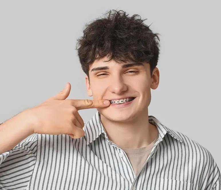 smiling young man metal braces light background after asking about "Will Braces Change My Face Shape?" - Will Braces Change My Face Shape? A Biomechanics PhD's Honest Answer | Limestone Hills Orthodontics Austin TX