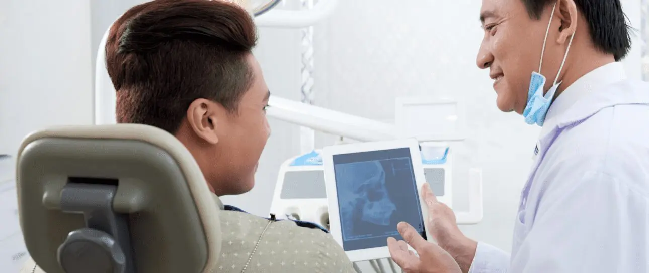 A dentist, who appears to be of Asian descent based on his features, shows a patient an X-ray on a tablet. Limestone Hills Orthodontics in Austin, TX, uses imaging for diagnosis.