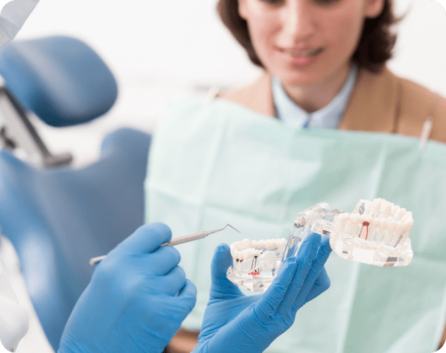 A gloved hand holds dental models and an instrument, explaining treatment to a patient in the background. Limestone Hills Orthodontics in Austin, TX, provides orthodontic consultations.