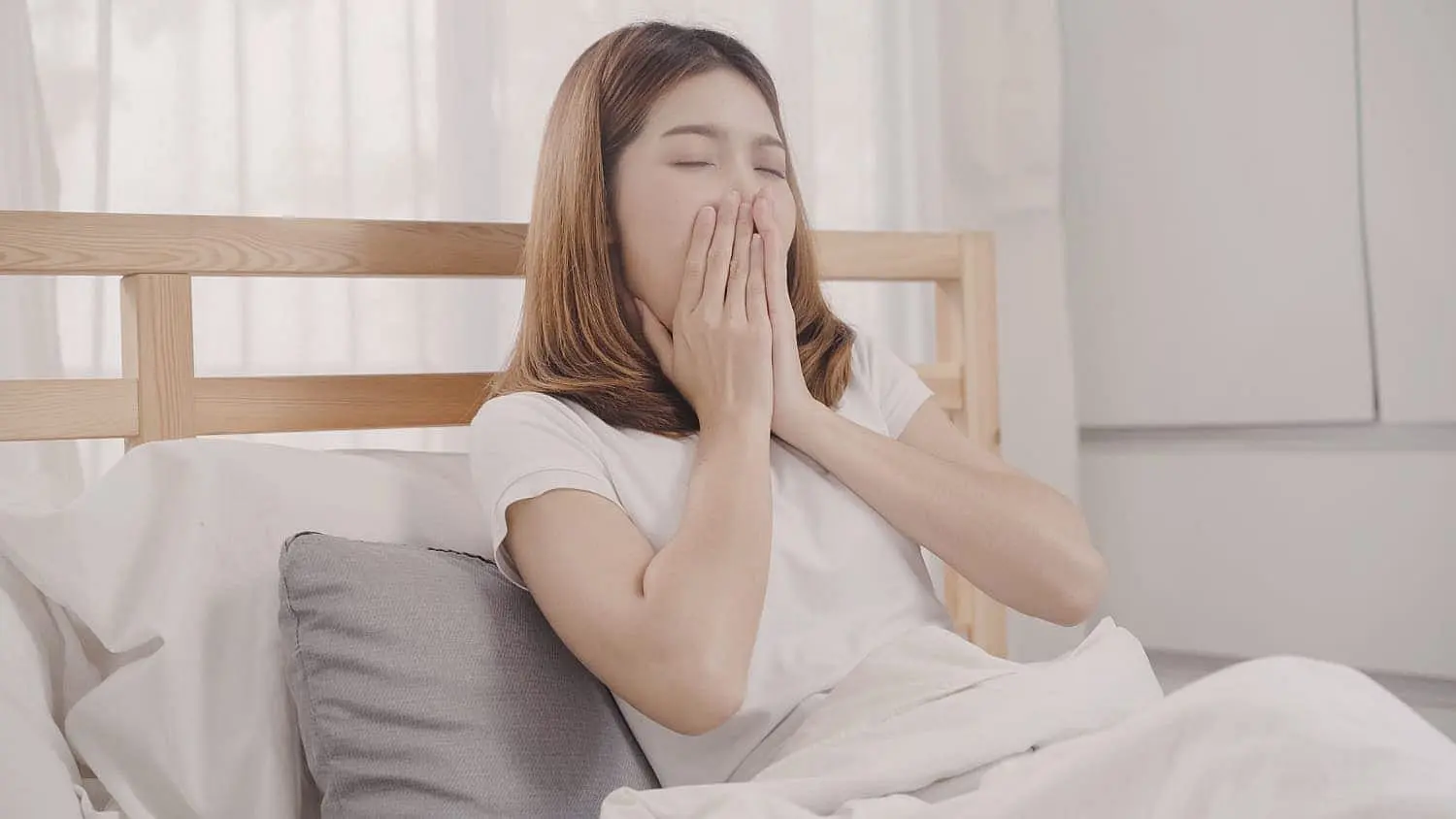 Woman yawning in bed, illustrating symptoms of sleep apnea and mouth breathing. Limestone Hills Orthodontics in Austin, TX provides information on the connection between mouth breathing and sleep apnea.
