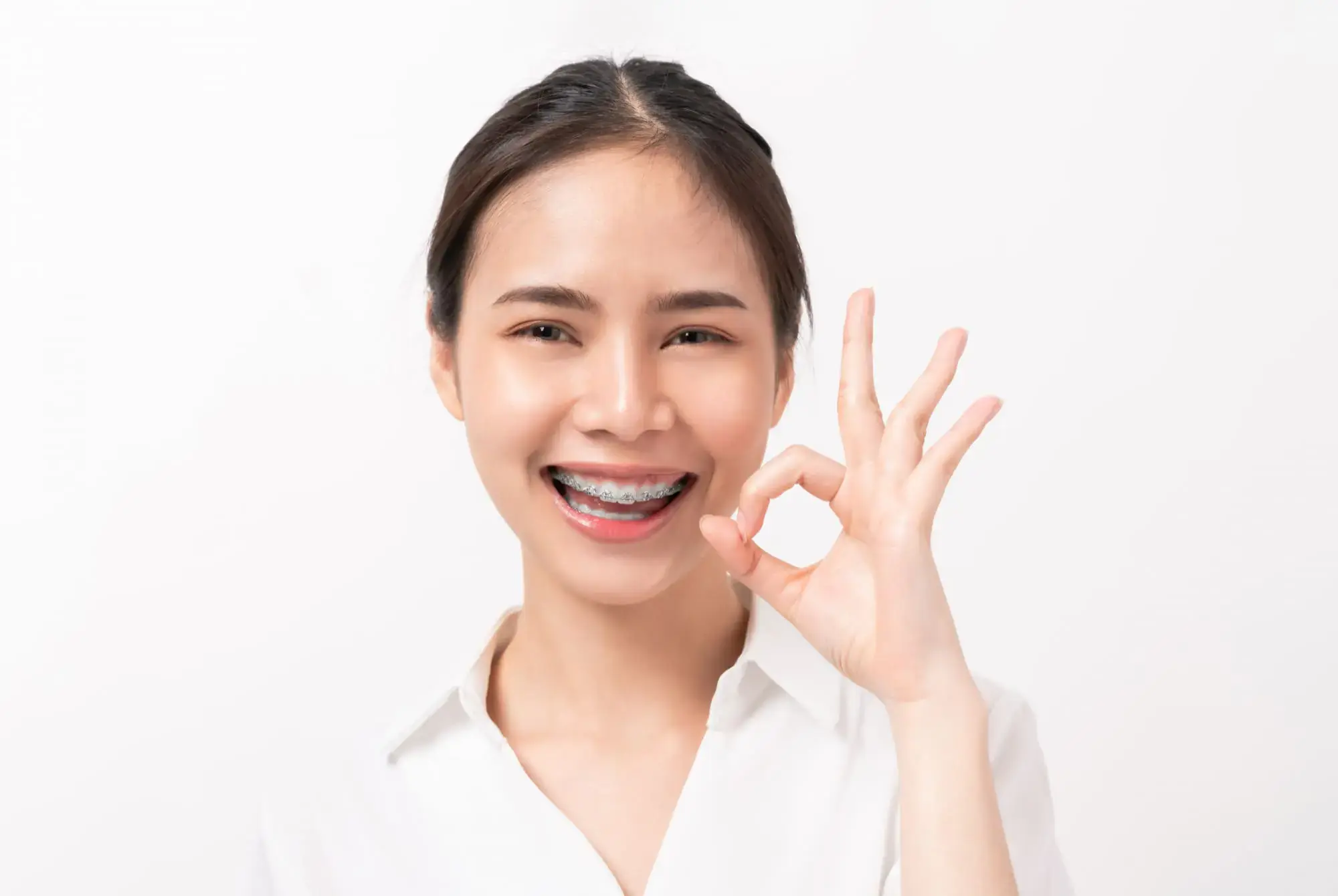 A young woman with ceramic braces smiles and gives an "OK" sign, representing Limestone Hills Orthodontics in Austin, TX. A young woman with ceramic braces smiles and gives an "OK" sign, representing Limestone Hills Orthodontics in Austin, TX.