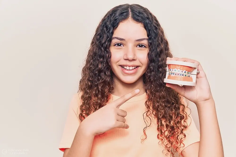 beautiful kid girl curly hair holding metal braces model showing Building Confidence with Orthodontics in Austin, TX