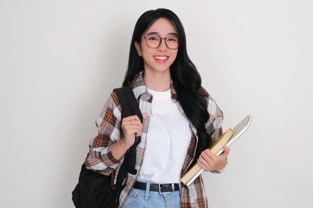A smiling college student carrying biology books and a backpack walks into Limestone Hills Orthodontics in Austin, TX, highlighting the available College Student Discount for Invisalign & Braces.