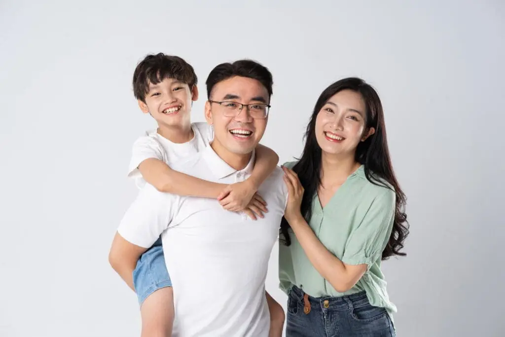 A man gives a piggyback ride to a smiling boy with braces while a woman stands beside them smiling after receiving family and sibling discounts at Limestone Hills Orthodontics in Austin, TX.