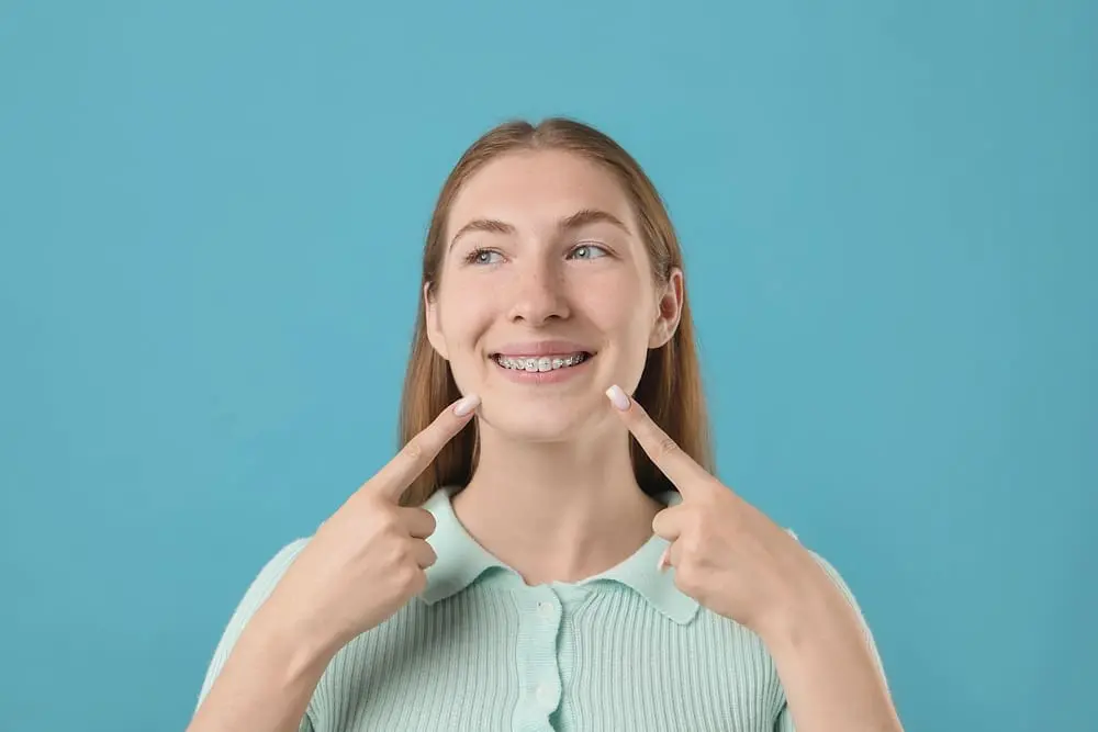 girl pointing her metal braces light blue background - MARPE and MSE Expanders: Palatal Expansion for Teens and Adults | Limestone Hills Orthodontics Austin TX