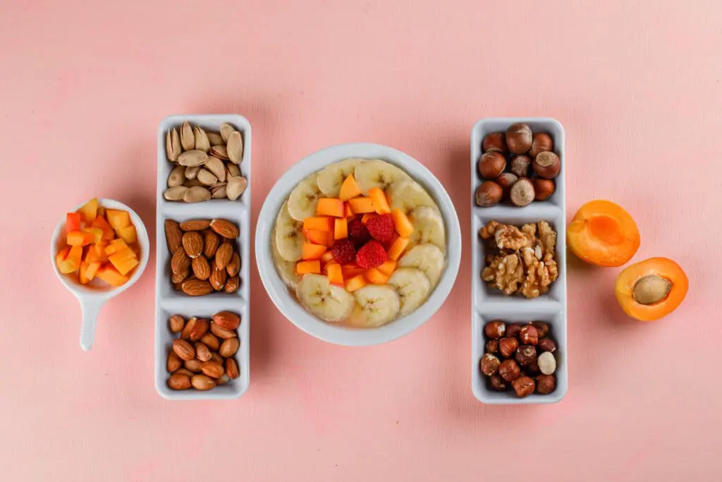 Oatmeal with banana, apricot, berries, nuts in a bowl on pink background, top view - Foods to Avoid with Braces: A Practical Family Guide