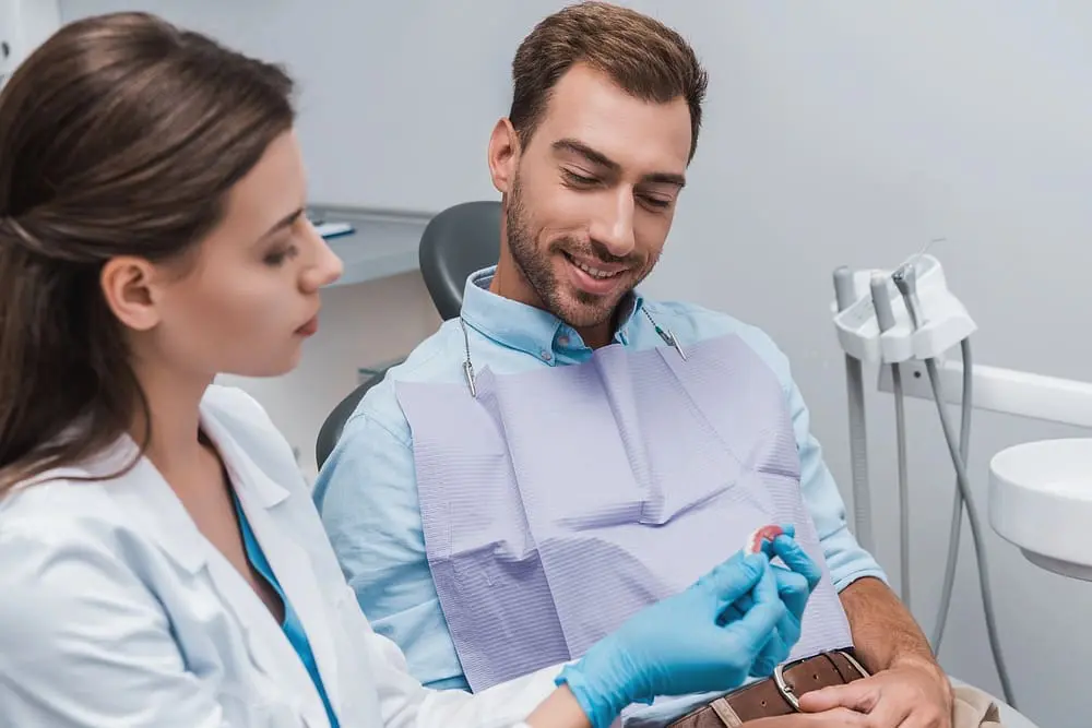 selective focus cheerful patient sitting dentist looking teeth model clinic - How to Maximize Orthodontic Insurance Benefits | Limestone Hills Orthodontics Austin TX