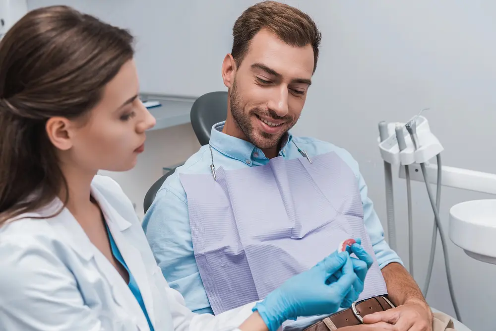 selective focus cheerful patient sitting dentist looking teeth model clinic - Orthodontist vs Dentist: What's the Difference? Limestone Hills Orthodontics Austin TX