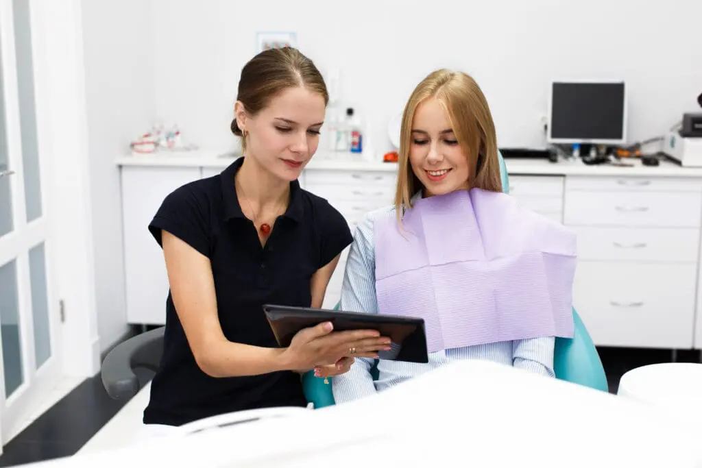 smiling woman sits chair dentist office while doctor shows her something - Orthodontic Payment Plans: Making Braces Affordable for Families | Limestone Hills Orthodontics Austin TX