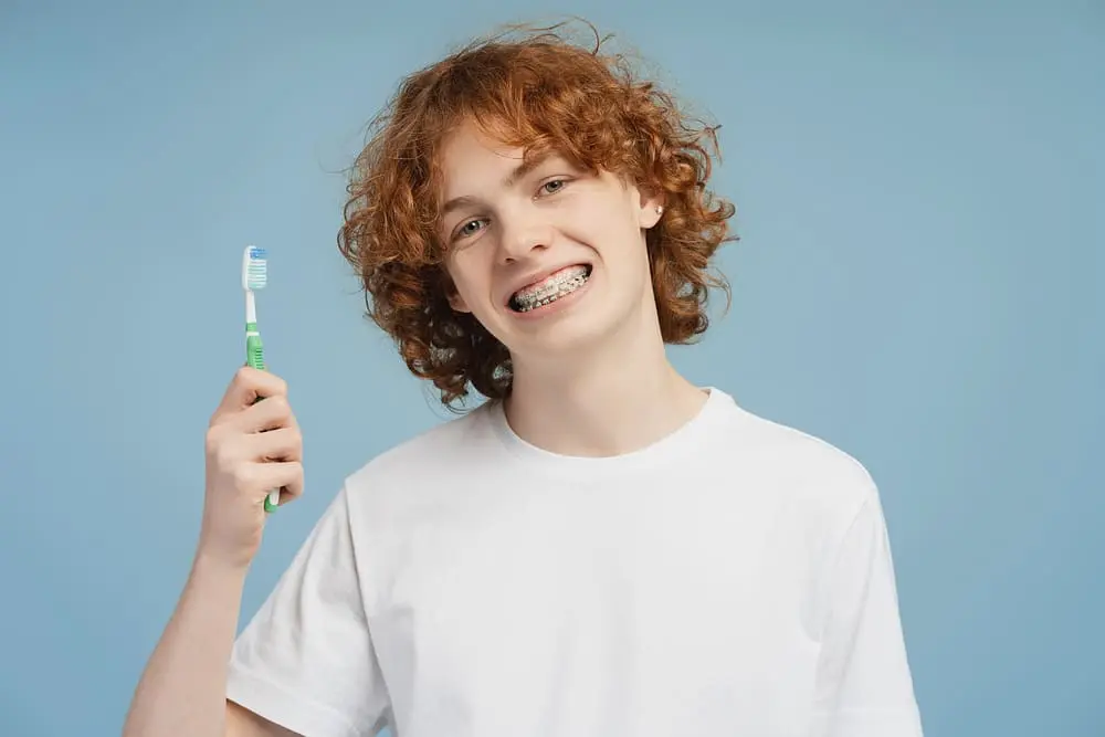 snapshot smiling metal braces wearing red head teen boy toothbrush hand isolated blue - How to Floss with Braces: A Step-by-Step Guide | Limestone Hills Orthodontics Austin TX