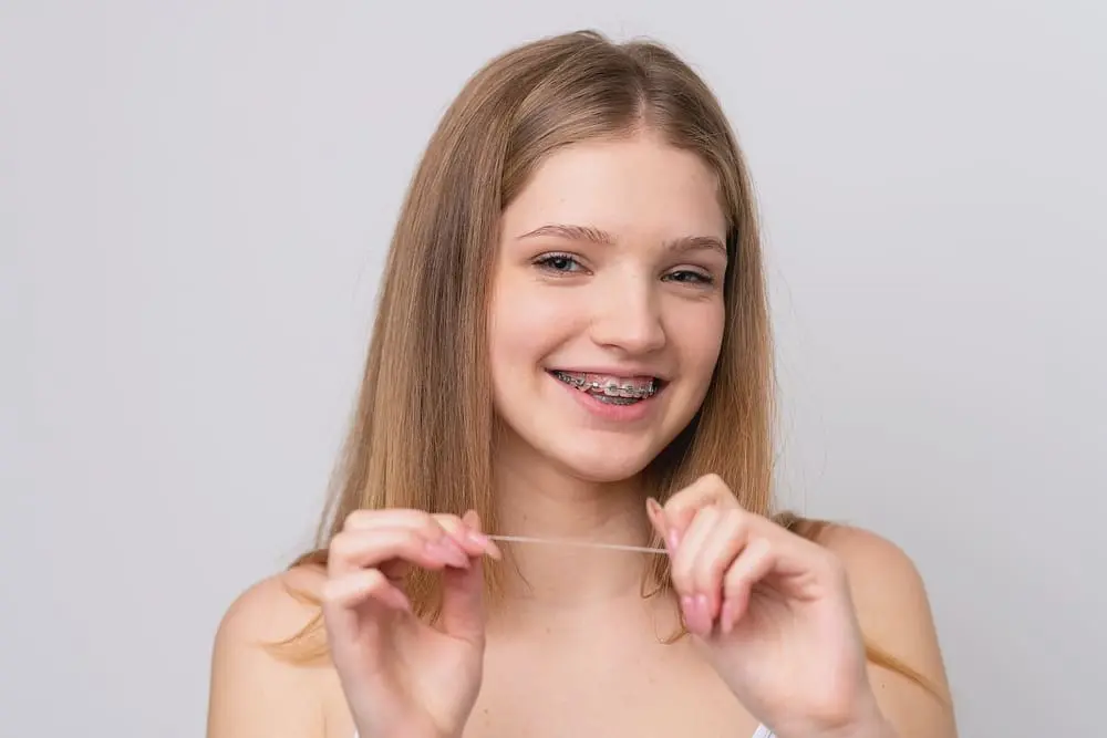 teenage girl with metal braces and floss isolaten white background - How to Floss with Braces: A Step-by-Step Guide | Limestone Hills Orthodontics Austin TX