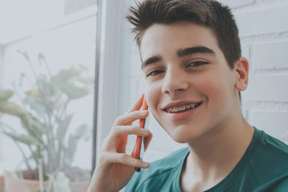 young man with metal braces talking mobile cell phone - Bruxism and Orthodontics: Can Braces Help Teeth Grinding? | Limestone Hills Orthodontics Austin TX