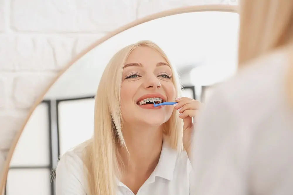 young woman metal braces toothbrush home - How to Floss with Braces: A Step-by-Step Guide | Limestone Hills Orthodontics Austin TX