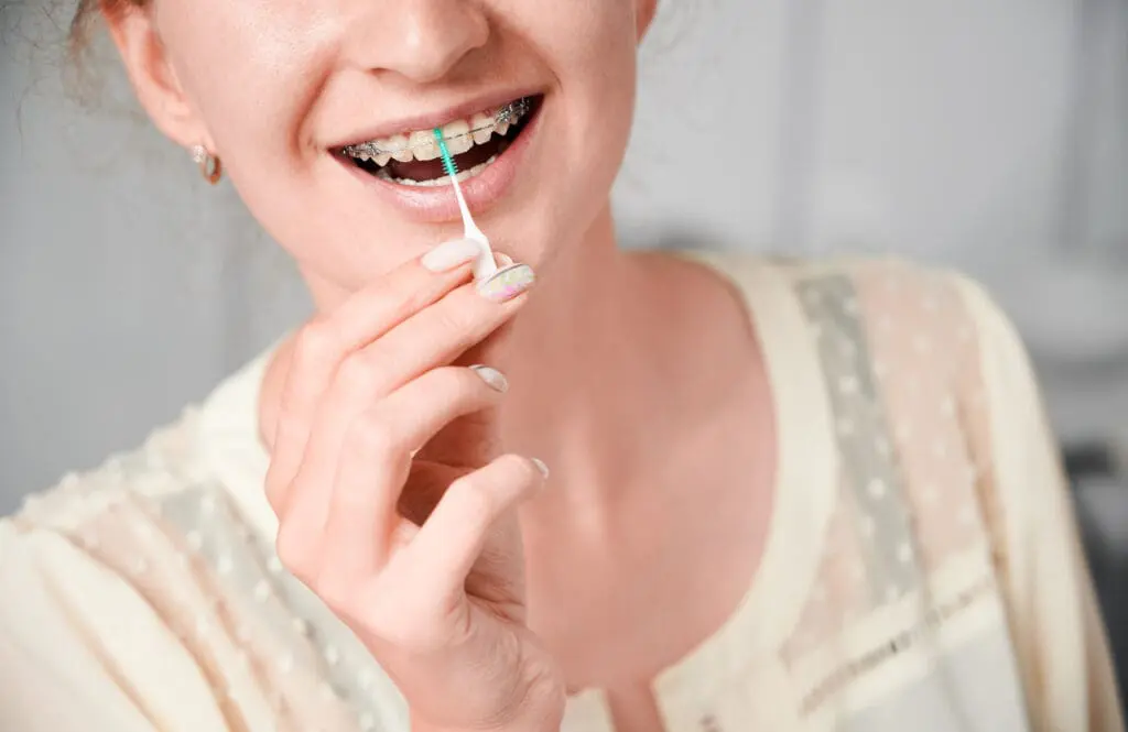 young woman with braces teeth using elastic cleaning toothpick - How to Clean Braces: Daily Routine, Tools, and Technique | Limestone Hills Orthodontics Austin TX