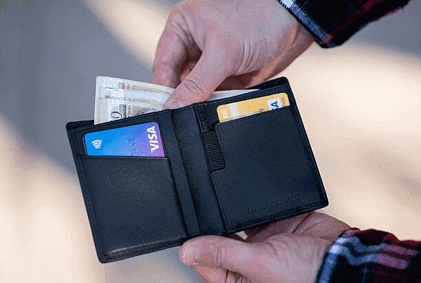 A person's hands hold a black bifold wallet containing cash and credit cards, including a Visa card. Limestone Hills Orthodontics in Austin, TX, offers various payment options.