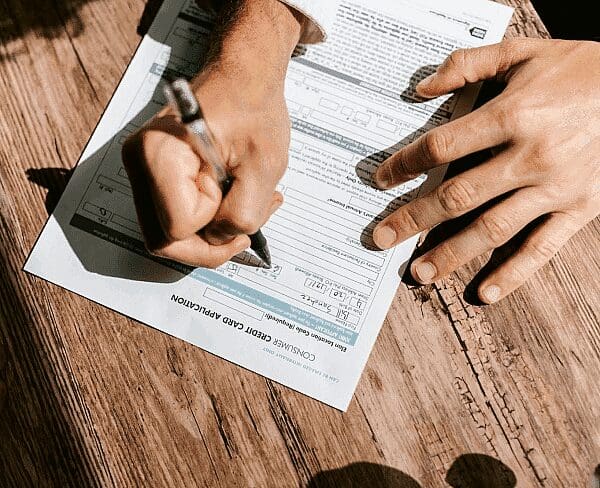 Hands fill out a "Consumer Credit Card Application" on a wooden surface. Limestone Hills Orthodontics in Austin, TX, may offer various payment options.